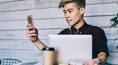 Japon hipster adam kulaklıkla müzik dinlerken akıllı telefon aygıtındaki bildirimi kontrol ediyor. Çinli blogcu cep telefonuyla sohbet ediyor netbook 'ta oturuyor ve oyuncuyu güncelliyor.
