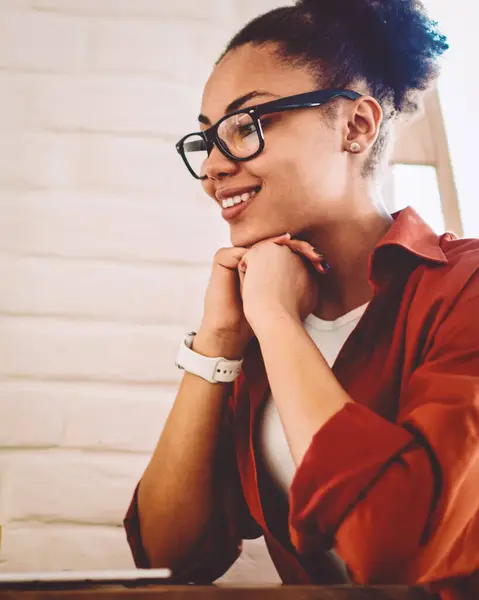 Happy black woman in optical eyewear for vision correction reading information in profile of famous blogger in social networks, cheerful hipster girl watching positive movie on content website