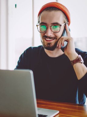 Neşeli hipster adamın portresi arkadaşlarıyla iş yerinde buluşup laptoptan öğrenme hakkında konuşuyor. Cep telefonuyla aradığı için internete bağlanan mutlu bir adam.