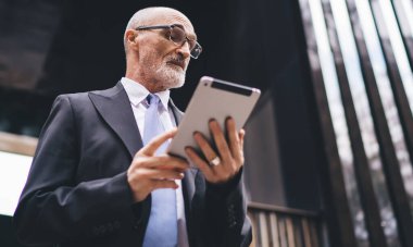 Resmi kıyafetli, gözlüklü ve beyaz sakallı yaşlı, yakışıklı, kel bir erkekten. İş merkezinin önündeki tabletlere göz atıyorlar.