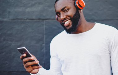 Tasasız genç erkek müzik sever. Kulaklıkla akıllı telefona bağlı kulaklıkla müzik listesinden en sevdiği sesi dinliyor. Açık havada oyuncu dinleyen pozitif hipster.
