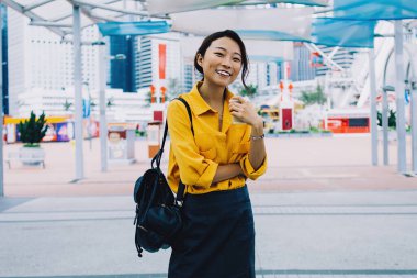 Şehir merkezinde durup kameraya gülümseyen, şık sırt çantalı kaygısız hippi kız ve Çin tatillerinin tadını çıkaran pozitif kadın turistin yarım boy portresi