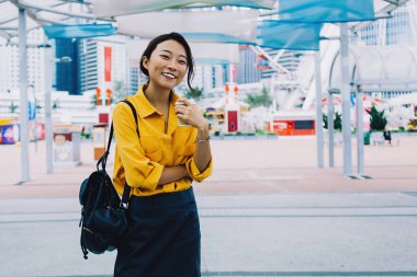 Şehir merkezinde durup kameraya gülümseyen, şık sırt çantalı kaygısız hippi kız ve Çin tatillerinin tadını çıkaran pozitif kadın turistin yarım boy portresi