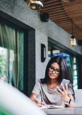 Gözlüklü düşünceli, beyaz bir kadın cep telefonu kullanan, cep telefonuyla ağlardan bilgi yazıyor. Kafe 'de cep telefonu ve kablosuz internet ile blog zaman geçirme fikirlerine dikkat çekiyor.