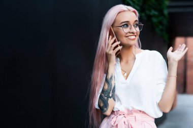 Genç, yaratıcı, uzun, parlak gül saçlı, şık yaz kıyafetleri giyen, cep telefonuyla konuşan ve gözlerini kaçıran bir kadın.