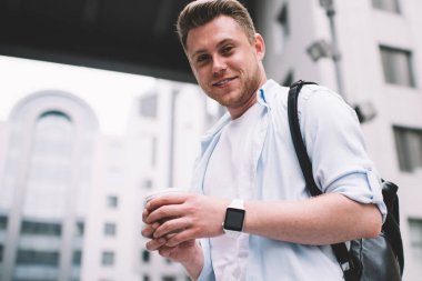 Elinde çantasıyla elinde kahve fincanı tutan ve sokakta kameraya gülümseyen yakışıklı milenyum adamından.