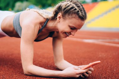 Sarışın, at kuyruklu çekici ve neşeli bir bayan stadyumda tahta örgü örüyor ve sosyal medyada bulanık arka planda gezinirken gülümsüyor.
