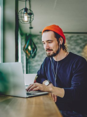 Kafkasyalı erkek, kafeteryada dinleniyor kulaklıkla favori müziği dinliyor ve sosyal ağlarda sohbet ediyor, yetenekli serbest yazar dizüstü bilgisayarında web günlüğü için yazı yazmaktan zevk alıyor.
