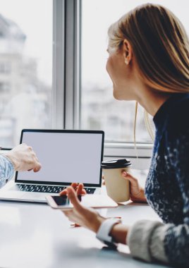 İki erkek ve kadın serbest çalışan ellerinde akıllı telefonla modern dizüstü bilgisayarda internet içeriğiniz için boş ekran alanı olan iş web sitelerini izliyorlar.