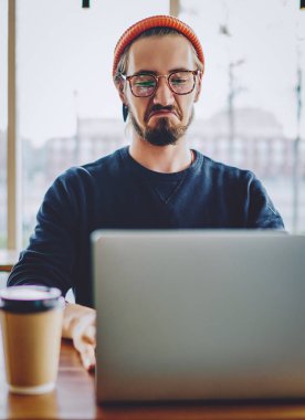 Erkek serbest çalışan kıskanç hissederken, dizüstü bilgisayarda internet bağlantısı olan şirketin web sitesinde ayın başarılı çalışanlarının derecelerini kontrol ediyor, hipster adam online video izliyor.