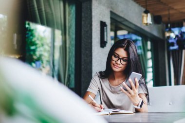 Gözlüklü düşünceli, beyaz bir kadın cep telefonu kullanan, cep telefonuyla ağlardan bilgi yazıyor. Kafe 'de cep telefonu ve kablosuz internet ile blog zaman geçirme fikirlerine dikkat çekiyor.