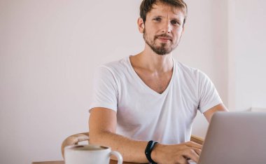 Modern dizüstü bilgisayarda uzaktan çalışan, kahve dükkanında oturan, kablosuz ücretsiz 4G internete bağlı, uzaktan kumandalı, yakışıklı erkek serbest çalışanın portresi.