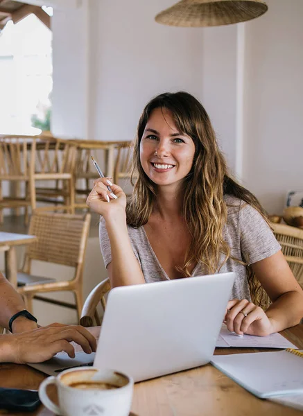 Smiling self-employed couple successfully working from home while woman creating ideas and writing down on paper and man carrying out on laptop