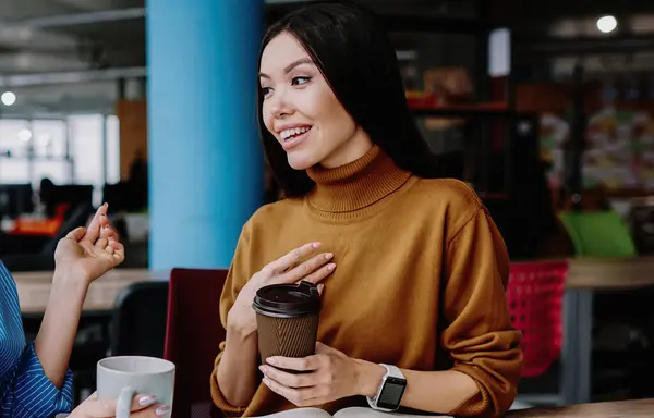 stock image Pretty caucasian female employees having fun communicating on break with coffee , prosperous women workers talking to each other smiling satisfied with cooperation sitting together at desktop