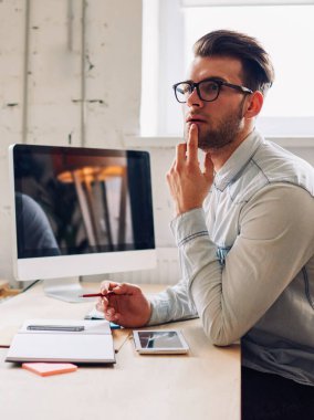 Gözlüklü, düşünceli, genç sakallı edebiyat öğretmeni ve modern sınıfta bilgisayarla aynı masada oturarak ilginç bir ders vermek için yaratıcı fikirler üzerinde düşünen bir adam.