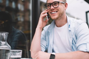 Gözlüklü yakışıklı bir genç kafenin terasında oturuyor ve mutlu bir şekilde gülümsüyor.