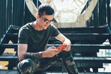 Genç Kafkasyalı, şık giyinmiş, şehir ortamını bekleyen ve oyun uygulamasını sohbet için akıllı telefon aygıtı kullanan genç, boş zamanlarında oynamak için kuran şık giyimli bir arkadaş.