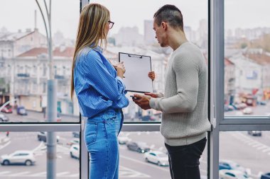 Bilgi içeren yetenekli bir sekreter, genç gururlu CEO 'nun modern ofis içinde büyük pencerelerle durduğu bir belge gösteriyor. İki profesyonel tasarımcı ortak görev üzerinde çalışan skeçleri tartışıyor.