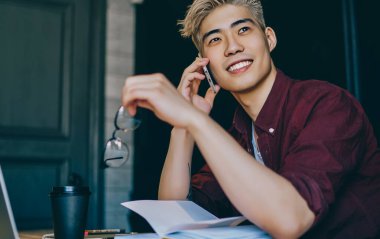 Hayalperest Çinli genç adam elinde gözlük tutuyor ve arkadaşlarıyla birlikte akıllı telefondan arıyor. Telefondan konuşan Japon hipster blogcu iş birlikçi dizüstü bilgisayarın başında oturmuş gülerken...