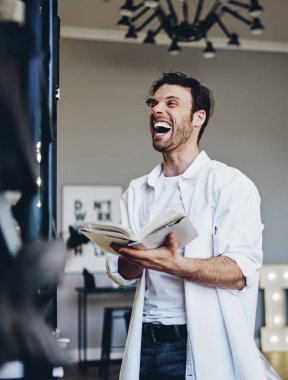 Keyfi yerinde beyaz bir erkek, evde edebiyat dergilerinden komik hikayeler okumaktan zevk alıyor. Mutlu hippi adam, evde boş zaman ve romandan tatmin olan kitaptan espirilere gülüyor.