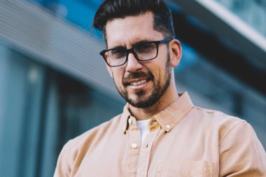 Modern iletişim teknolojisi olan yakışıklı beyaz adamın portresi. Şehir ortamında dikilip poz veren, optik gözlüklü akıllı telefon kullanıcısı kameraya bakıyor.