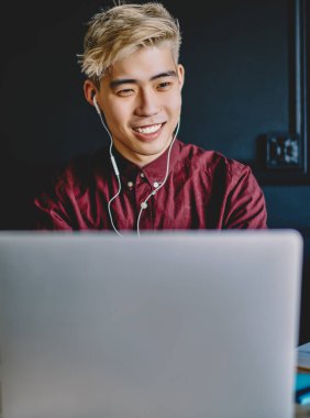 Sıradan giyinmiş neşeli Çinli hippi internet sitesinde internet bağlantısı kullanarak dizüstü bilgisayara bağlı dijital kulaklıklarla müzik dinliyor. Modern uzayda masaüstünde otururken