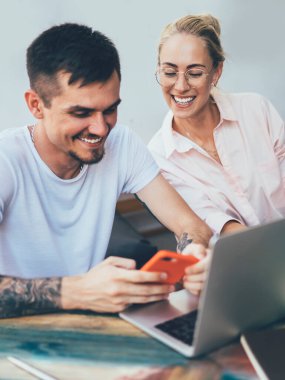 Gündüz vakti şık bir kafede ilham kaynağı bulmak için akıllı telefon ve defter kullanan gülümseyen genç iş arkadaşları.