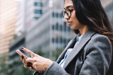 Gözlüklü, siyah, uzun saçlı, New York caddesinde yürüyen ve cep telefonu kullanan çekici genç iş kadını.