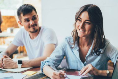 Gülümseyen kadın, bayan meslektaşıyla konuşuyor ve not defterine not alıyor. Masada memnun bir adamla oturuyor. Laptop dokümanları ve kafeterya terasında aletleri var.
