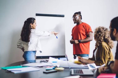 Modern, çok ırklı genç kadın ve erkekler sınıf odasında birlikte vakit geçirip beyaz tahtada proje yazma fikri üzerinde çalışıyorlar.