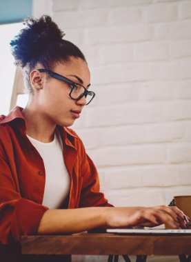 Ciddi koyu tenli, serbest çalışan bir kadının modern netbook 'ta online programlama arayışının yan görüntüsü. Yetenekli Afro-Amerikan hippi kız dizüstü bilgisayar aygıtıyla veri tabanı oluşturuyor.