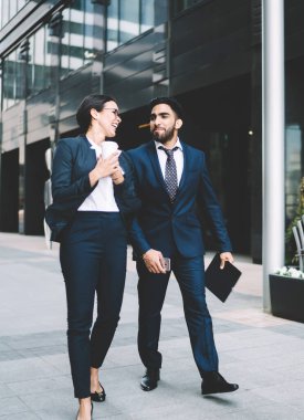 Katı siyah takım elbiseli çok kültürlü iş arkadaşları yazın şehir merkezinde ellerinde cep telefonu klasörlü kahveyle yürüyorlar.