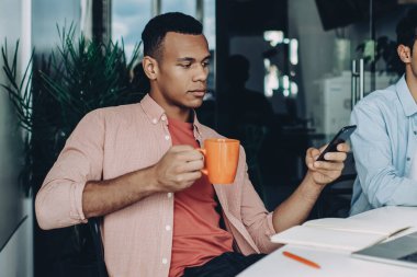 Çalışma saatlerinde modern teknolojiyi kullanan çok kültürlü erkek meslektaşlar 4G kablosuz internete bağlı, yetenekli programcı cep telefonu web sitesinde finans haberleri okuyor.