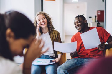 Bir grup modern etnik çeşitlilikte genç insan aydınlık ofis salonunda toplanıyor ve yeni proje fikri üzerinde kafa patlatırken kağıtları tartışıyorlar.