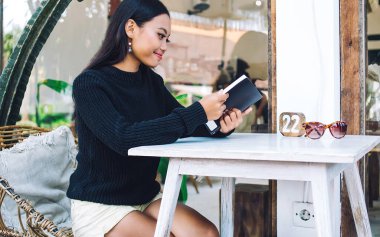 Bali 'deki kafenin terasında otururken siyah saçlı güzel Endonezyalı bir kadının menü kitabının yan görüntüsü.