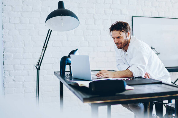 Серьезный мужчина фрилансер, проверяющий публикацию в блоге на ноутбуке, работающий удаленно, кавказский бизнесмен, работающий в современном интерьере коворкинга пространства читать новости и доход по электронной почте на нетбуке