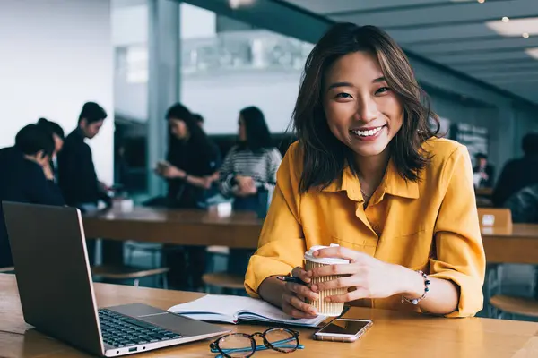 Masaüstünde dizüstü bilgisayarla oturan mutlu bir bayan öğrencinin portresi. Öğrenim sırasında kendini iyi hissediyor. Kafein içeceği tutan ve içeride gülen mutlu Japon serbest yazar.