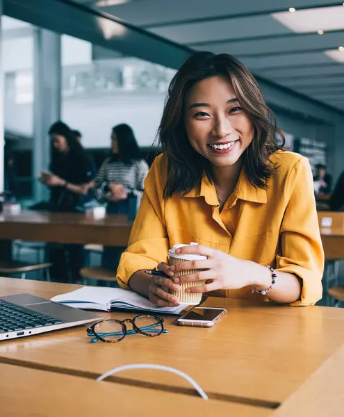 Masaüstünde dizüstü bilgisayarla oturan mutlu bir bayan öğrencinin portresi. Öğrenim sırasında kendini iyi hissediyor. Kafein içeceği tutan ve içeride gülen mutlu Japon serbest yazar.