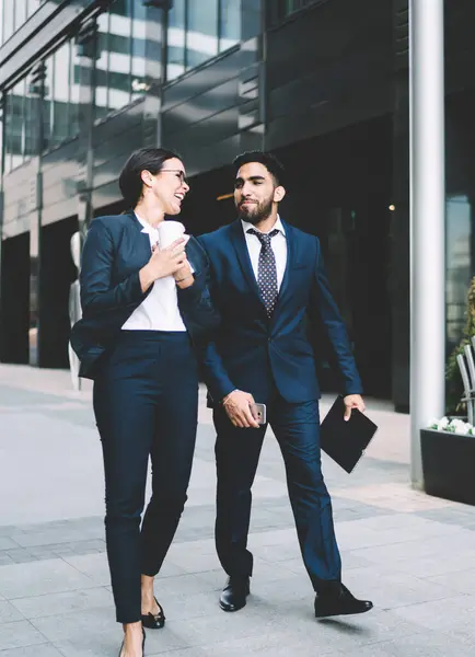 Katı siyah takım elbiseli çok kültürlü iş arkadaşları yazın şehir merkezinde ellerinde cep telefonu klasörlü kahveyle yürüyorlar.
