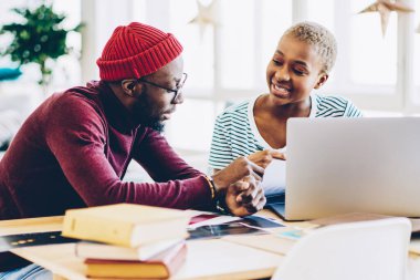 Modern iç mekanda masaüstünde oturan yaratıcı fikirleri ve planları tartışan meslektaşlar, Apartman dairesinde dizüstü bilgisayar kullanarak iletişim kurmayı öğrenen ve kullanan Afro-Amerikan öğrenciler