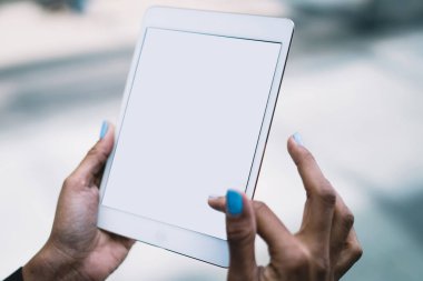 Siyah elbiseli, turkuaz manikürlü, beyaz tablet kaydırma ekranı kullanan ve gündüz vakti sokakta bilgi arayan kimliği belirsiz bir kadın.