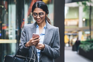 Şık giyinmiş, gözlüklü, gülen iş kadını New York sokaklarında yürürken deri çanta taşıyan sörf arabası tutuyor.