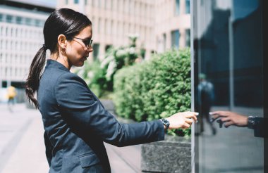 Güneşli bir günde modern şehrin sokaklarında reklam panosu kullanan resmi takım elbiseli ve gözlüklü ciddi genç bayanın yan görüntüsü.