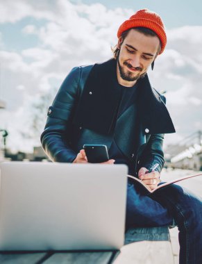 Bilgi kitaplarına sahip pozitif bir erkek öğrenci internet sitesinde cep telefonuyla bilgi okuyor. Reklam alanında çalışırken, modaya uygun giyinmiş beyaz bir adam arkadaşlarıyla sohbet ediyor.