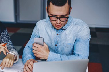 Gündelik kıyafet giyen iki öğrenci dizüstü bilgisayarlarında ders izliyorlar ve modern ofiste not defteriyle birlikte oturuyorlar. Genç adam ve kadının işbirliği ile ortak çalışma projesi hazırlıyorlar.
