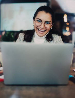 Gözlüklü ve günlük kıyafetlerle gezen neşeli serbest yazar camından bilgisayarını kullanarak kafede oturup kameraya bakarak projenin başarısının tadını çıkar.