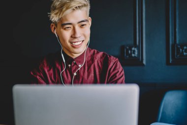 Sıradan giyinmiş neşeli Çinli hippi internet sitesinde internet bağlantısı kullanarak dizüstü bilgisayara bağlı dijital kulaklıklarla müzik dinliyor. Modern uzayda masaüstünde otururken