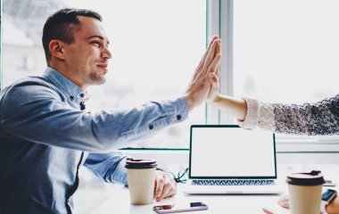 Başarılı genç erkek ve bayan meslektaşlar, internet içeriğiniz için boş ekran alanı olan modern dizüstü bilgisayarla masada yaptıkları toplantıda, harika bir iş için birbirlerine beş tane iş veriyorlar.