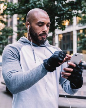 Sakallı, mesaj yazan ve müzik dinleyen siyah bir sporcu. Eğitimde ara verildiğinde kulaklık takıyor. Bulanık arka planda sokakta yürürken.