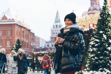 Samimi palto ve fularlı genç kadınlar ellerinde bir fincan kahveyle şehir caddesinde parlayan köknar ağaçları ve çelenklerle yeni yılın tadını çıkarıyorlar.